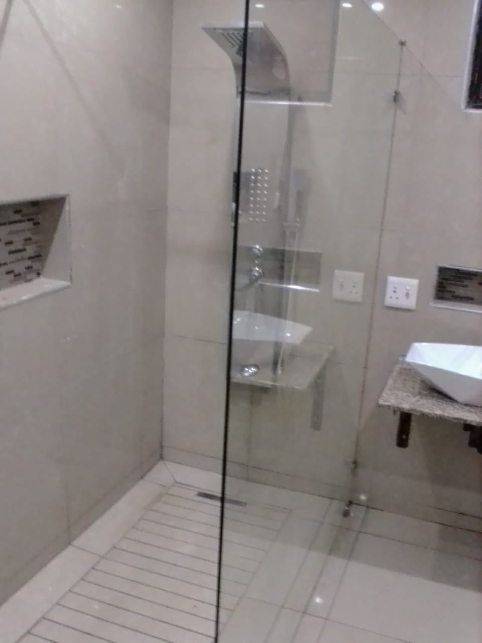 A tiled shower with a glass screen and a wall-mounted shower panel