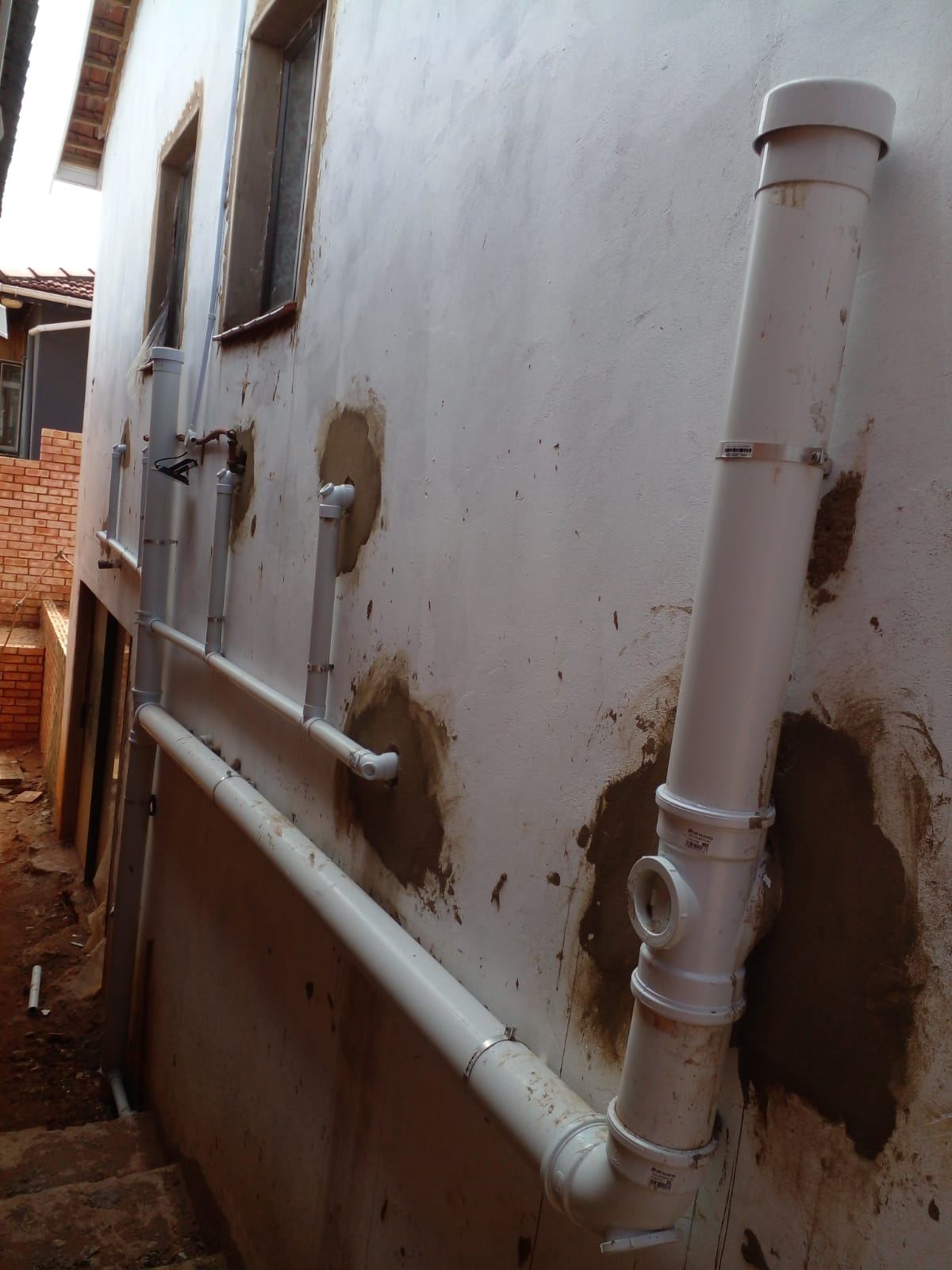A white drainage stack and branch pipes fixed to the outside wall of a house
